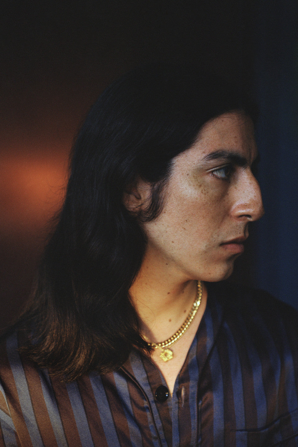 Man with long hair and a gold necklace against a dark background